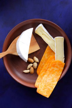 Camembert peyniri, turuncu peynir, fıstık, tahta kaşık ve spatula ile kil ware vintage tarzı bir koyu mavi arka plan üzerinde