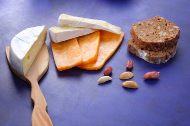 Camembert peyniri, turuncu peynir, fıstık, tahta spatula ve ekmek tahıl üzerinde vintage tarzı bir koyu mavi arka plan ile