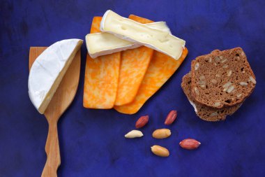 Camembert peyniri, turuncu peynir, fıstık, tahta spatula ve ekmek tahıl üzerinde vintage tarzı bir koyu mavi arka plan ile