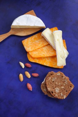 Camembert peyniri, turuncu peynir, fıstık, tahta spatula ve ekmek tahıl üzerinde vintage tarzı bir koyu mavi arka plan ile