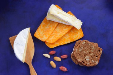 Camembert peyniri, turuncu peynir, fıstık, tahta spatula ve ekmek tahıl üzerinde vintage tarzı bir koyu mavi arka plan ile
