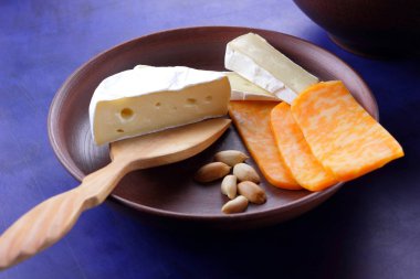 Camembert peyniri, turuncu peynir, fıstık, tahta kaşık ve spatula ile kil ware koyu mavi zemin üzerine