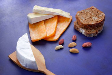 Camembert peyniri, turuncu peynir, fıstık, tahta spatula ve ekmek tahıl üzerinde koyu mavi arka plan ile