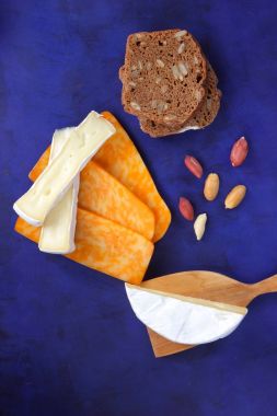 Camembert peyniri, turuncu peynir, fıstık, tahta spatula ve ekmek tahıl üzerinde koyu mavi arka plan ile