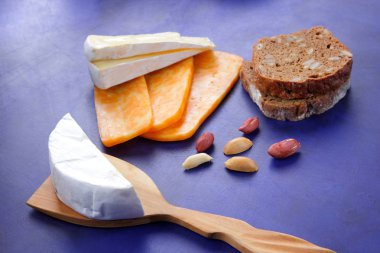 Camembert peyniri, turuncu peynir, fıstık, tahta spatula ve ekmek tahıl üzerinde koyu mavi arka plan ile