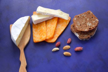 Camembert peyniri, turuncu peynir, fıstık, tahta spatula ve ekmek tahıl üzerinde koyu mavi arka plan ile