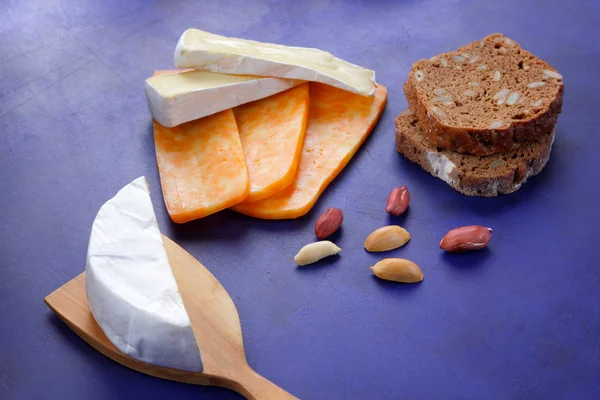 Camembert peyniri, turuncu peynir, fıstık, tahta spatula ve ekmek tahıl üzerinde koyu mavi arka plan ile