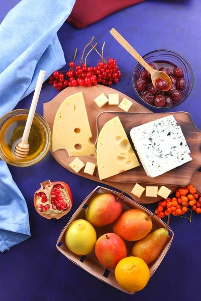 Different cheeses, lemon, pomegranate, mandarin, pears, berries, honey, jam, cheese with a mold on a wooden board in the style of pop art and retro style, Christmas cheese — Stock Photo, Image