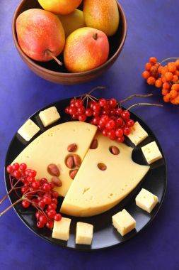 Sert peynir peynir kırmızı meyveler, fıstık, kartopu, minimalizm tarzı peynir, peynir ve retro tarzı bir koyu mavi arka plan üzerinde kırmızı meyveler siyah bir tabakta delikli