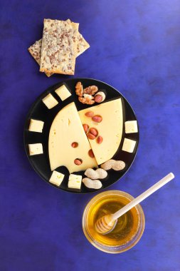 Sert peynir peynir fıstık, tatlım, bisküvi, ceviz, minimalizm tarzı, peynir koyu mavi zemin üzerine beyaz peynir ile siyah bir tabakta delikli