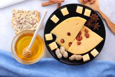 Sert peynir, peynir siyah bir plaka üzerinde delikli, peynir, bal ve fındık, tarçın ve bir kova ile Noel yemeği peynir bal beyaz bir arka planda hafif bir arka plan üzerinde fındık ile peynir dilimleri ile