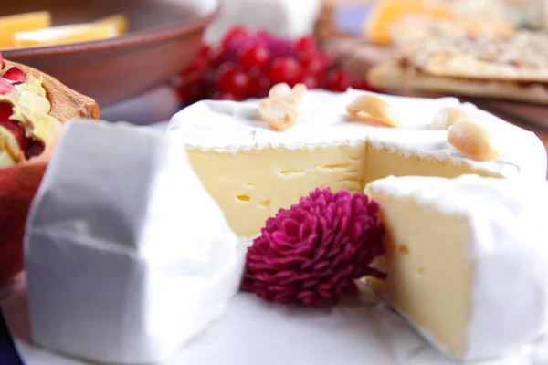 Cheese, soft camembert cheese, red berries, pomegranate, peanut grains, flower, biscuits, white cheese on a blue background, wooden board, pop art, retro style