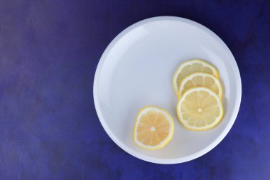 Ultraviyole bir arka planda beyaz tabakta vegan, taze limon limon dilimli vitaminler, minimalizm narenciye stil, pop art, koyu mavi arka plan ile meyve