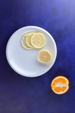 Ultraviyole bir arka planda beyaz tabakta vegan, taze limon limon dilimli vitaminler, minimalizm narenciye stil, pop art, koyu mavi arka plan ile meyve