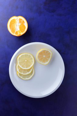 Ultraviyole bir arka planda beyaz tabakta vegan, taze limon limon dilimli vitaminler, minimalizm narenciye stil, pop art, koyu mavi arka plan ile meyve