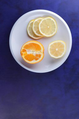 Ultraviyole bir arka planda beyaz tabakta vegan, taze limon limon dilimli vitaminler, minimalizm narenciye stil, pop art, koyu mavi arka plan ile meyve