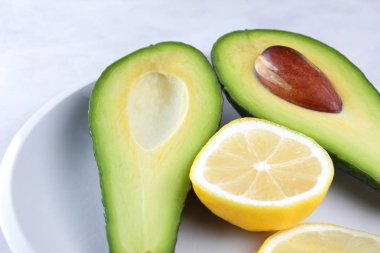 Avokado ve beyaz bir plaka üzerinde beyaz bir arka plan, yeşil ve sarı meyve, tropikal meyve, dilimlenmiş avokado ve mermer arka plan, sağlıklı gıda, vegan, minimalizm limon limon dilimleri