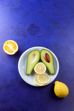 Avokado, limon ve beyaz bir plaka üzerinde yarım portakal, bir ultraviyole arka plan, vejetaryen Kahvaltı, Asya Mutfağı, avokado pop art, narenciye, turuncu avokado ile tropikal meyveler