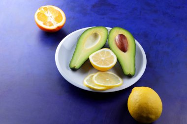 Avokado, limon ve beyaz bir plaka üzerinde yarım portakal, bir ultraviyole arka plan, vejetaryen Kahvaltı, Asya Mutfağı, avokado pop art, narenciye, turuncu avokado ile tropikal meyveler