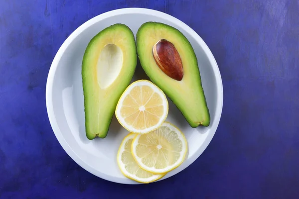 Aguacate Rodajas Limón Plato Blanco Frutas Tropicales Sobre Fondo Ultravioleta — Foto de Stock