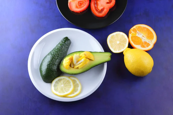 Avocado and lemon on a white plate, tomato on a black plate, citrus on an ultraviolet background, chopped banana and pear, avocado pop art, healthy food, vegan, retro style