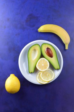 Avokado, muz, limon ve yeşil armut beyaz tabakta, tropikal meyve bir ultraviyole arka plan, vejetaryen Kahvaltı, Asya Mutfağı, avokado pop art, narenciye, muz ve avokado, sanat ile armut