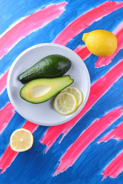 Avocado and lemon on a rosy blue background, tropical fruits, citrus on a white plate, fruit on a pop art background, vegan, healthy food