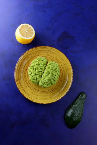 Avocado and lemon, pasting of sandwiches with avocado on a yellow plate on the ultraviolet background, green spread made with avocado, half a lemon, vegetarian food, pop art, Latin American cuisine