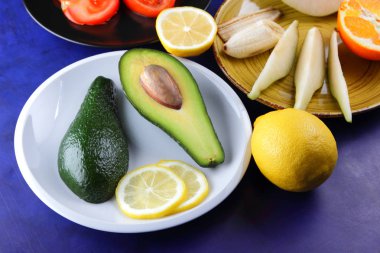 Limon beyaz tabakta domates siyah plaka, ultraviyole bir arka planda, narenciye ve avokado doğranmış muz ve armut, avokado pop art, sağlıklı gıda, vegan, pop art