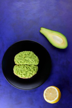 Avokado ve limon, sandviç yayılan ultraviyole arka planda, yeşil ile yapılan avokado, yarım limon, vejetaryen yemek, pop art, Latin Amerika mutfağı ile ekmek, siyah plaka üzerinde avokado Yapıştır