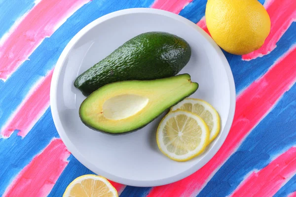 Avocado and lemon on a rosy blue background, tropical fruits, citrus on a white plate, fruit on a pop art background, vegan, healthy food, avocado pop art