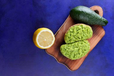 Avokado ve limon ekmek üzerinde bir tahta masa, avokado yapıştırırken, ahşap tahta sandviç yayılan ultraviyole arka planda, yeşil ile yapılan avokado, yarım limon, vejetaryen yemek, Latin Amerika mutfağı ile