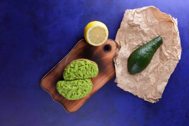 Avokado ve limon ekmek üzerinde bir tahta masa, avokado yapıştırırken, ahşap tahta sandviç yayılan ultraviyole arka planda, yeşil ile yapılan avokado, yarım limon, vejetaryen yemek, Latin Amerika mutfağı ile