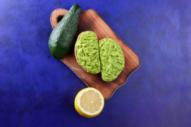 Avokado ve limon ekmek üzerinde bir tahta masa, avokado yapıştırırken, ahşap tahta sandviç yayılan ultraviyole arka planda, yeşil ile yapılan avokado, yarım limon, vejetaryen yemek, Latin Amerika mutfağı ile
