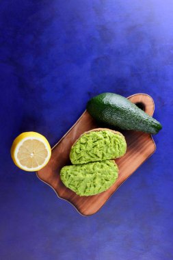 Avokado ve limon ekmek üzerinde bir tahta masa, avokado yapıştırırken, ahşap tahta sandviç yayılan ultraviyole arka planda, yeşil ile yapılan avokado, yarım limon, vejetaryen yemek, Latin Amerika mutfağı ile
