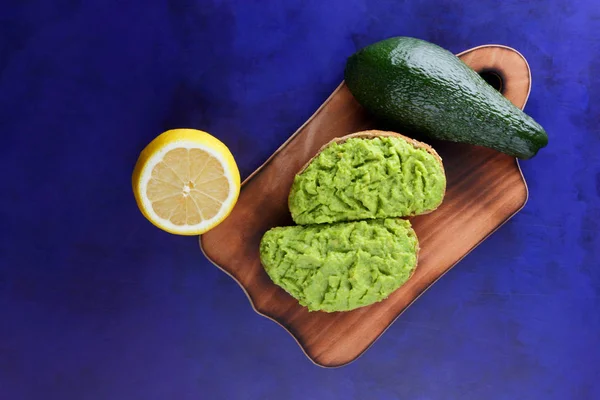 Avokado ve limon ekmek üzerinde bir tahta masa, avokado yapıştırırken, ahşap tahta sandviç yayılan ultraviyole arka planda, yeşil ile yapılan avokado, yarım limon, vejetaryen yemek, Latin Amerika mutfağı ile