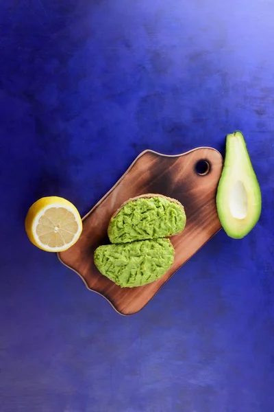 Avocado and lemon on a wooden board, avocado paste on bread, wood board with sandwiches on the ultraviolet background, green spread made with avocado, half a lemon, vegetarian food, Latin American cuisine