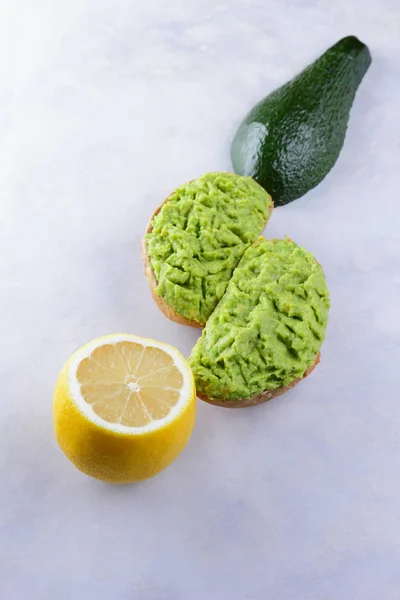 Avocado, lemon and sandwiches with avocado paste on white background, half of green avocado and lemon, copy space, sandwiches with pasta with avocado, exotic fruits, vegan, diet food, mexican cuisine