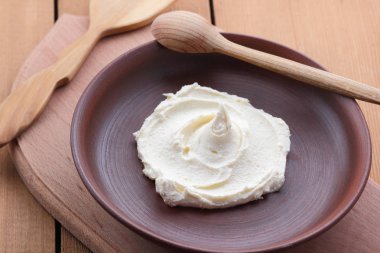 Ekşi krema krem bir plaka, süt tatlı bir tahta kaşık, vegan, basit gıda, ahşap bir masa üzerinde bir kil tabakta retro tarzı süt model, rustik tarzı, süt ürünleri, kopya alanı