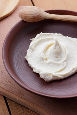 Ekşi krema krem bir plaka, süt tatlı bir tahta kaşık, vegan, basit gıda, ahşap bir masa üzerinde bir kil tabakta retro tarzı süt model, rustik tarzı, süt ürünleri, kopya alanı