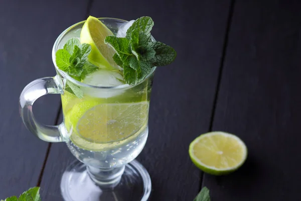 Mojito on a dark background, summer cocktail with lime, refreshing drink with lemon, fresh mint for cocktail, celebratory drink with ice, vegan, copy space, minimalist cocktail
