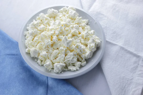 Cheese, cottage cheese on a white plate, fresh cottage cheese on a white and blue napkin, dairy product on a white background, healthy food, French breakfast, top view, goat curd in minimalist style, protein