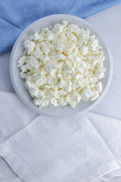 Cheese, cottage cheese on a white plate, fresh cottage cheese on a white and blue napkin, dairy product on a white background, healthy food, French breakfast, top view, goat curd in minimalist style, protein