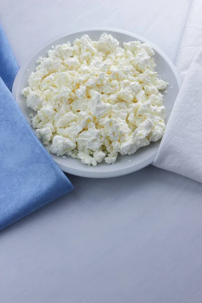 Cheese, cottage cheese on a white plate, fresh cottage cheese on a white and blue napkin, dairy product on a white background, healthy food, French breakfast, top view, goat curd in minimalist style, protein