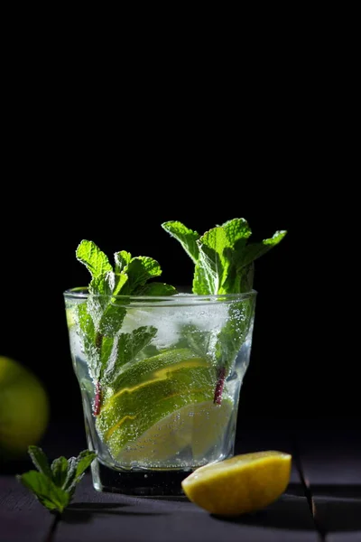 Mojito on a dark background, summer cocktail with lime and mint, refreshing drink with lemon, fresh mint for cocktail, celebratory drink with ice, vegan, copy space, minimalist cocktail, blank for designer, bar