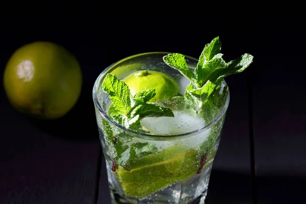 Mojito on a dark background, summer cocktail with lime and mint, refreshing drink with lemon, fresh mint for cocktail, celebratory drink with ice, vegan, copy space, minimalist cocktail, blank for designer, bar