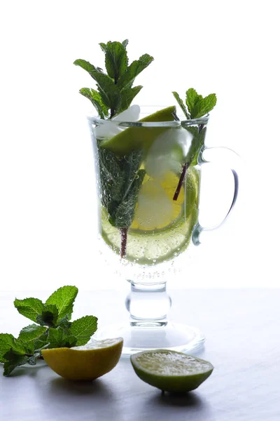 Cocktail with ice on a white background, mojito on summer vacation, a soft drink with lime and lemon, fresh mint for a cocktail, citrus for making a drink, minimalism, preparation for a designer