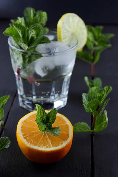 Mojito on a dark background, summer cocktail with lime and mint, refreshing drink with lemon, fresh mint for cocktail, celebratory drink with ice, vegan, copy space, minimalist cocktail, blank for designer, art