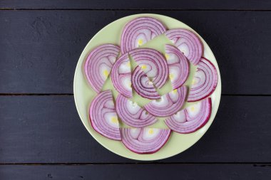 Menekşe yay soğan soğan dilimlenmiş karanlık bir ahşap zemin üzerine yeşil bir tabakta sebze rustik tarzı, minimalizm, vejetaryen ürün, vitaminler, sağlıklı gıda, sanat bir tabağa ortaya koydu