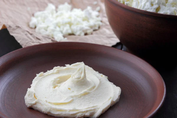 Cheese, fresh cottage cheese and sour cream in earthenware, goat curd on parchment paper, dairy products on a wooden background in rustic style, healthy food, copy space, cottage cheese on a dark background, minimalism